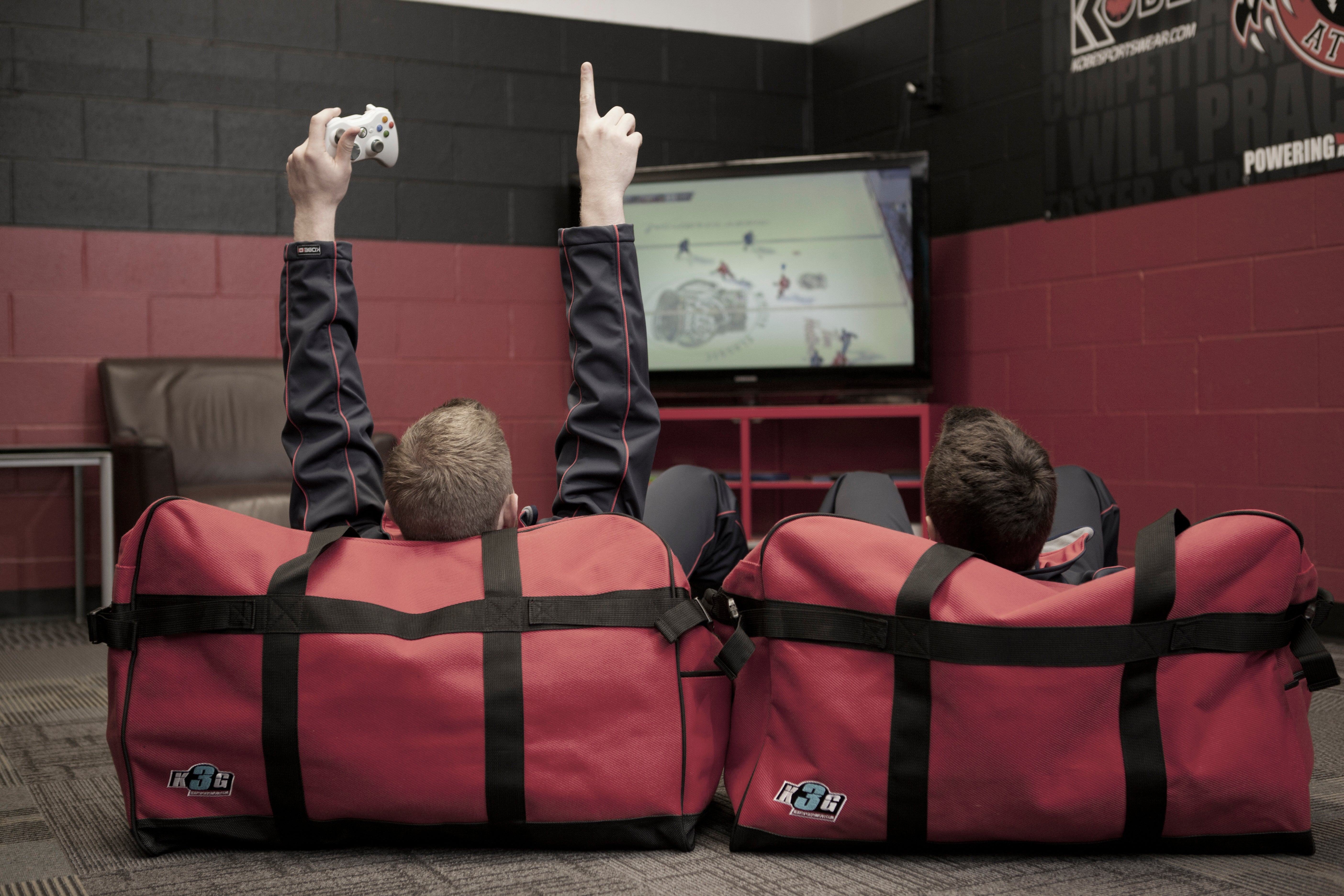 Two people sitting in red kobesportswear bags with black straps, watching a screen in a room with a brick wall.