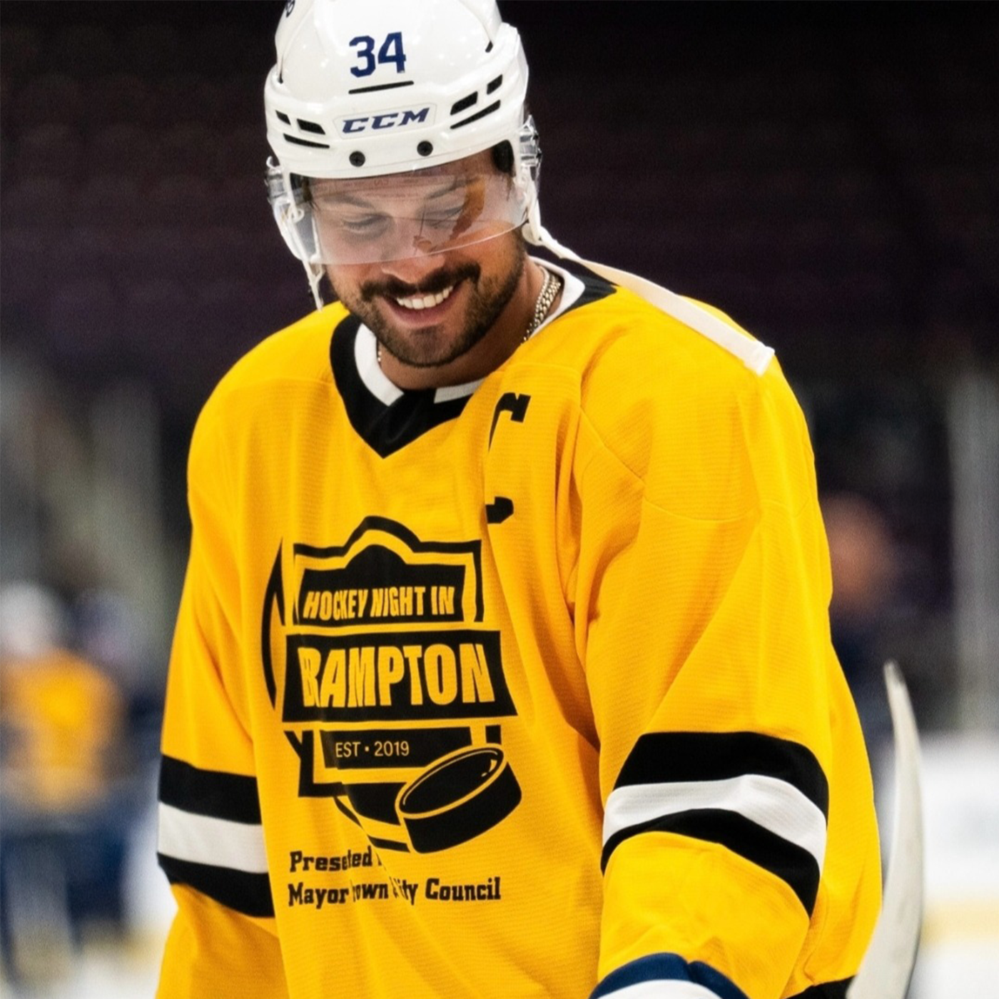 Hockey player wearing a Kobesportswear yellow jersey with 'Hockey Night in Rampton' text on an ice rink.